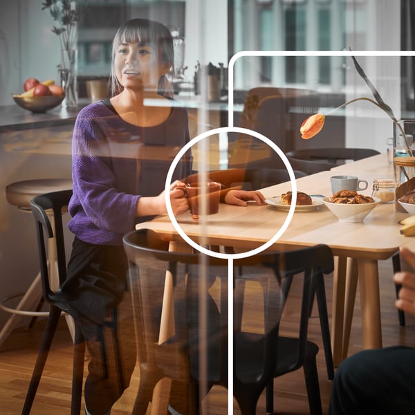 Nainen istuu pöydän ääressä ikkunalasin takana.