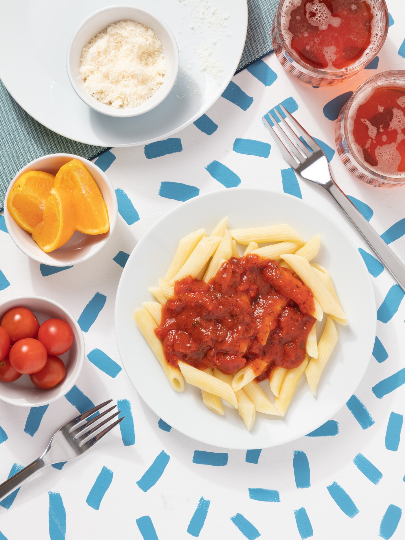 A table with white and blue tablecloth, white plates with pasta and tomato sauce