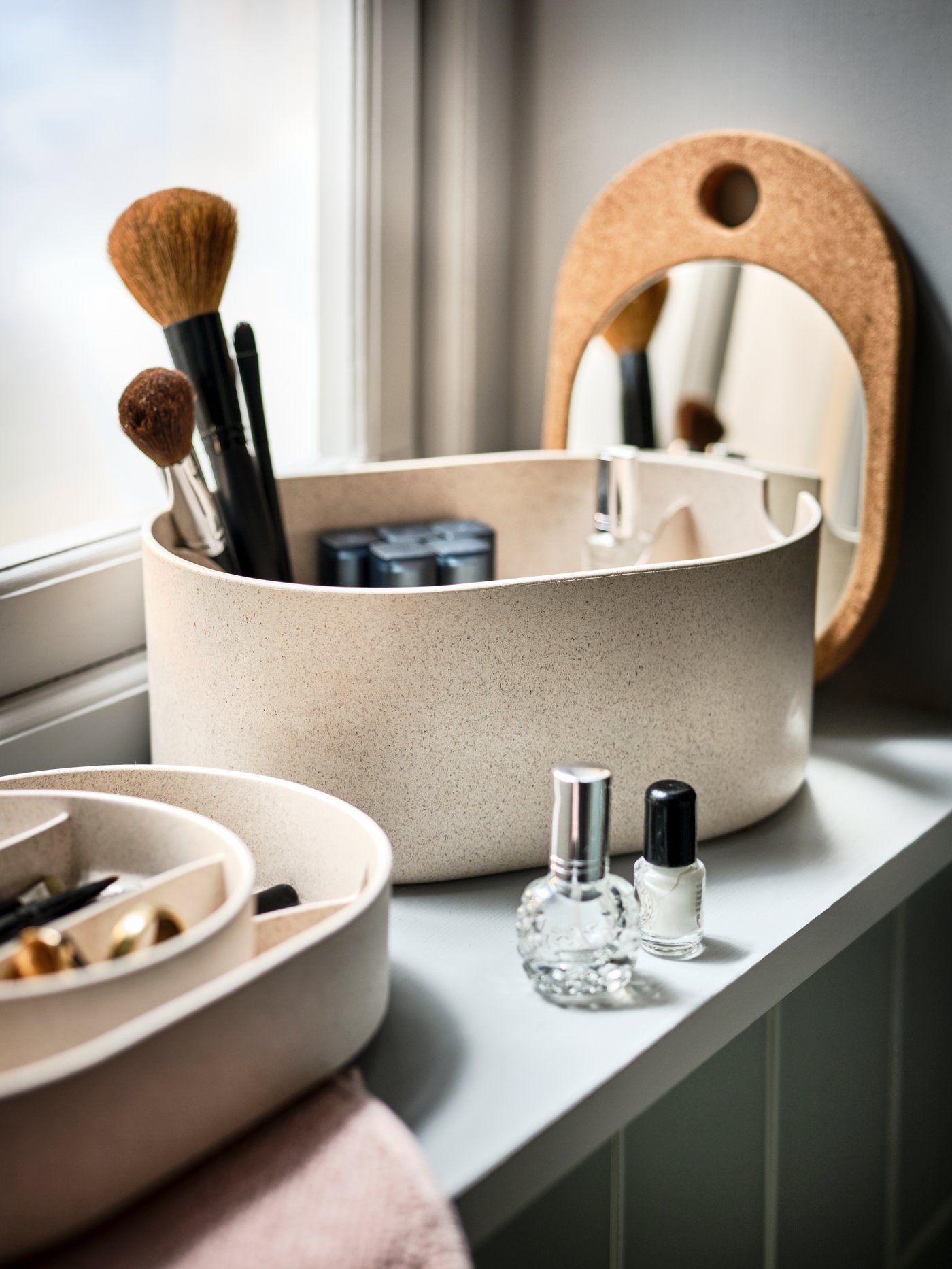 Un alféizar de un baño con una caja de almacenaje SAXBORGA con espejo, llena y rodeada de accesorios de maquillaje.
