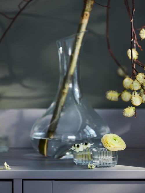 Dormitor dulap cu carafă de sticlă care deține ramură înflorit și suporturi elegante din sticlă tealight cu flori decorative mici.