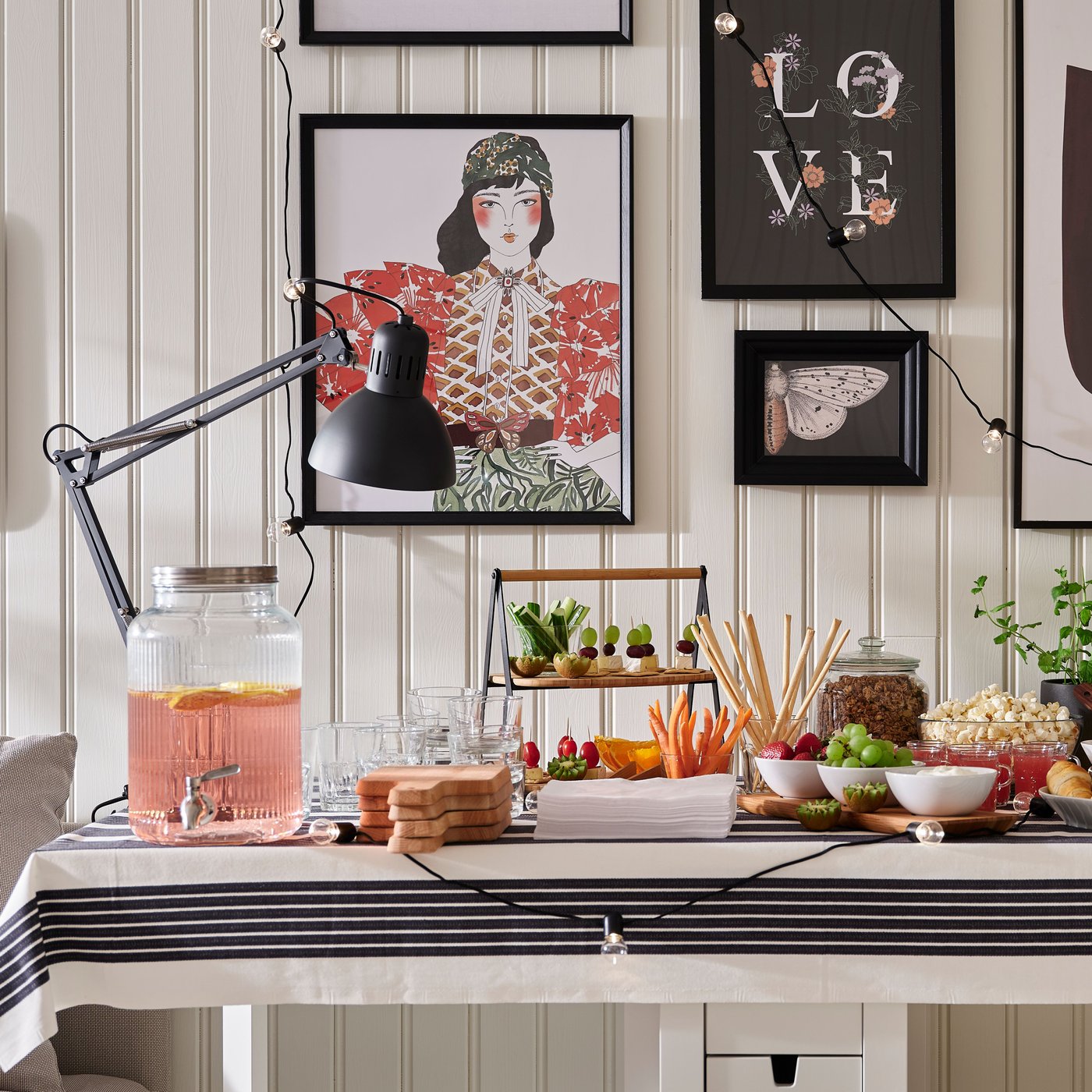 Dukat bord med dryck, kakor, frukt och grönsaker. I bakgrunden syns tavlor och ljusslingor på väggen.