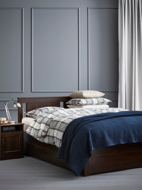 Bedroom with brown bed frame, bedside table, duvet cover, two pillowcases, bedspread, curtains, cushion cover, work lamp.