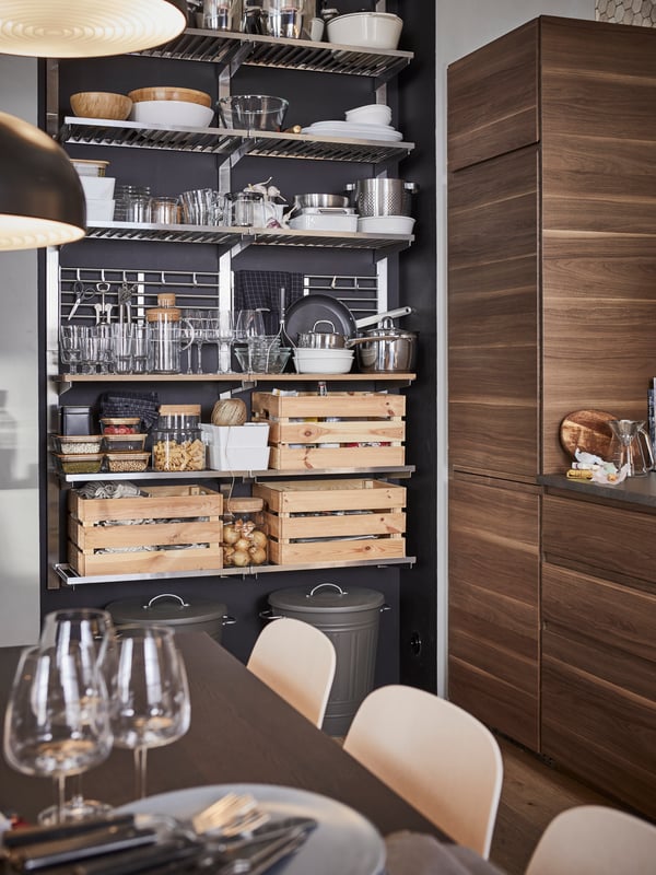 A kitchen with a stainless steel open storage shelving unit storing containers, tableware and three boxes in pine.