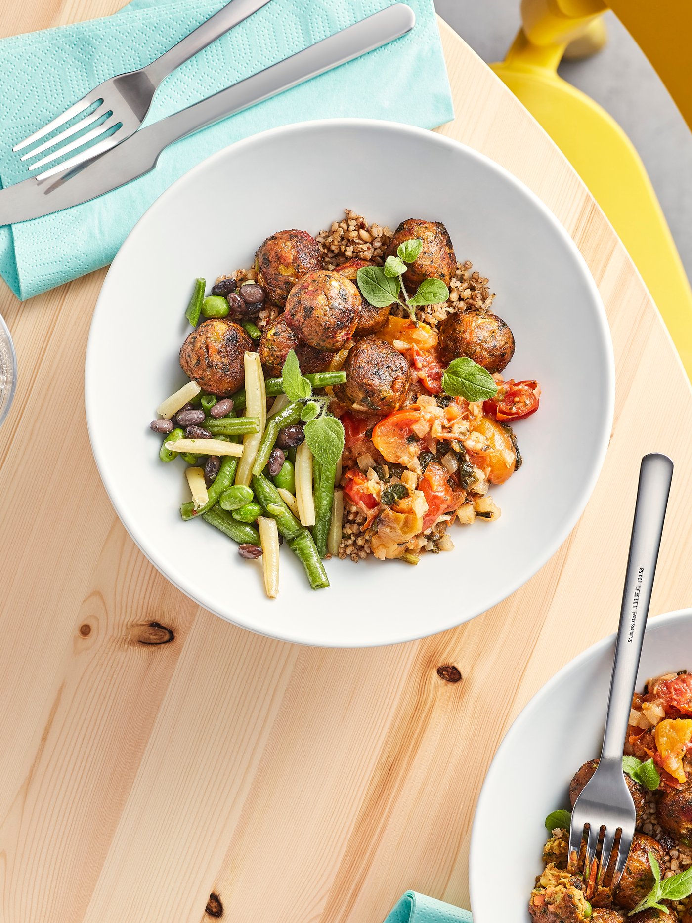 A wooden table with napkins, cutlery and two white plates with plant balls and a colourful mix of cooked vegetables.