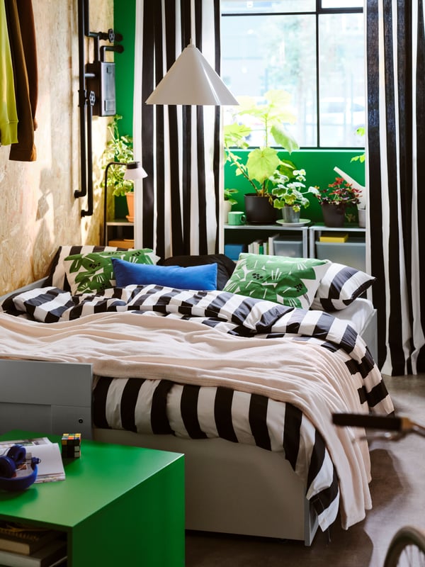 Un letto divano con due cassetti BRIMNES grigio aperto e trasformato in un letto matrimoniale con biancheria da letto SLÅNHÖSTMAL nero/bianco/a righe.