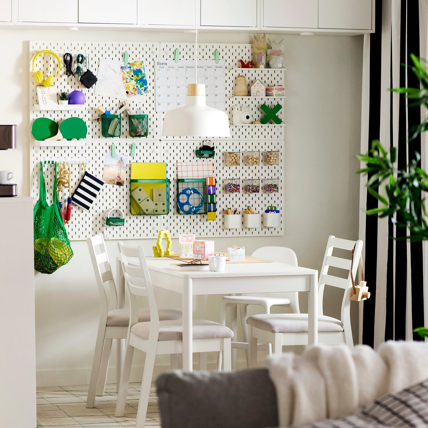 A room with a TONSTAD extendable table in white, four TONSTAD chairs, an ANTILOP highchair and a pegboard on the wall.