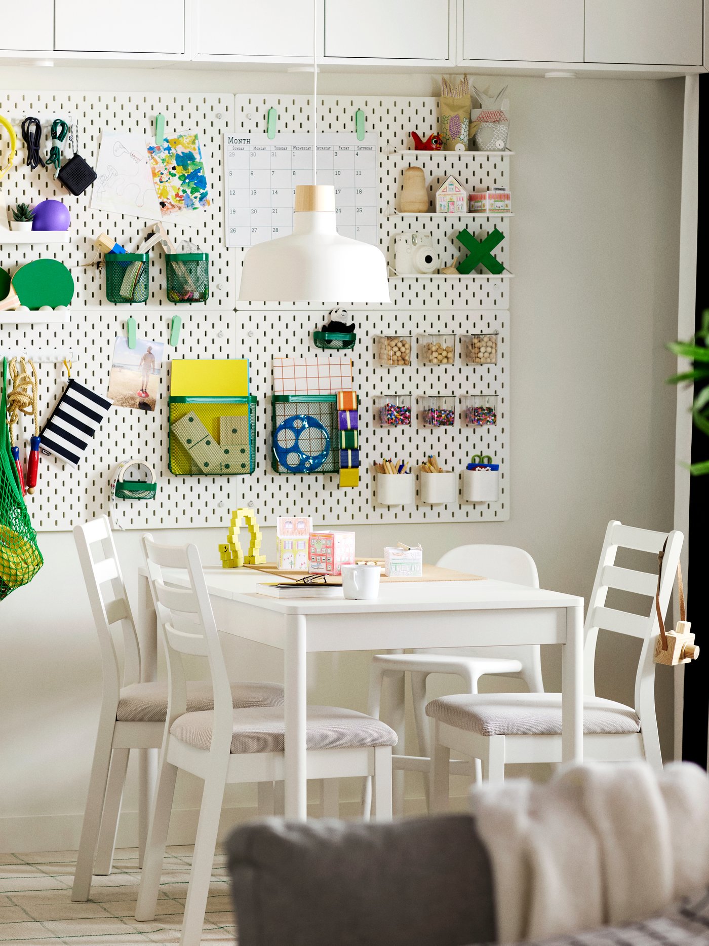 An off-white TONSTAD extendable table surrounded by four white chairs, set in a bright dining area with wall-mounted storage.