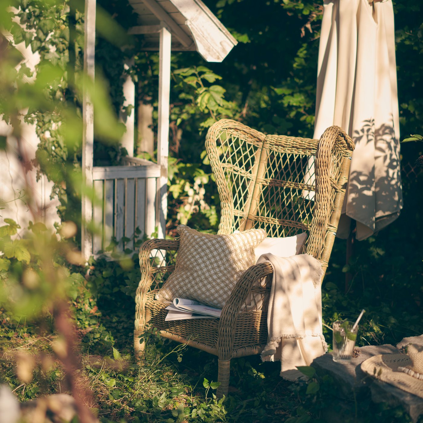 En rottingmöbel står i en grönskande trädgård.