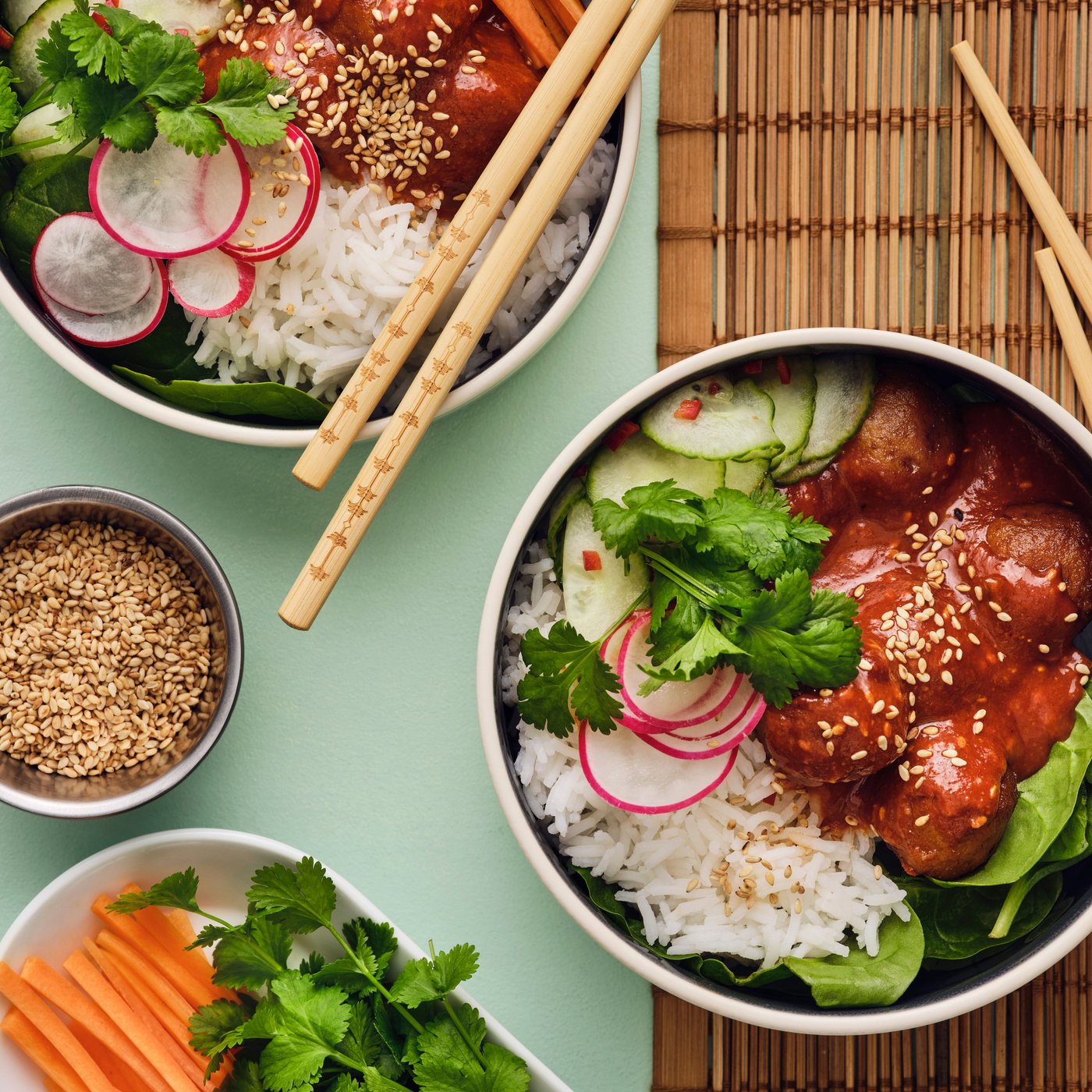 Two white bowls are placed on a table, and they are filled with a salad made of meatballs, cucumber and other vegetables.