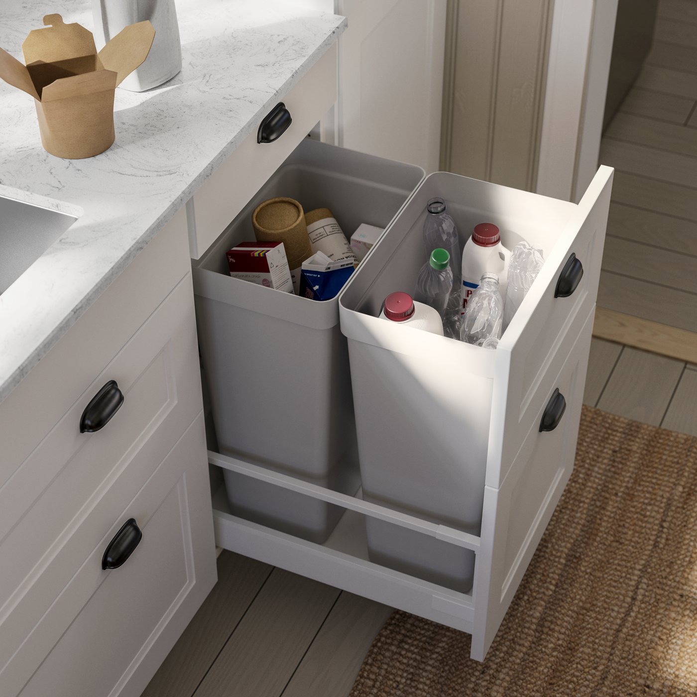 A kitchen featuring a white system with grey countertops, showcasing two grey bins filled with various recyclable containers.