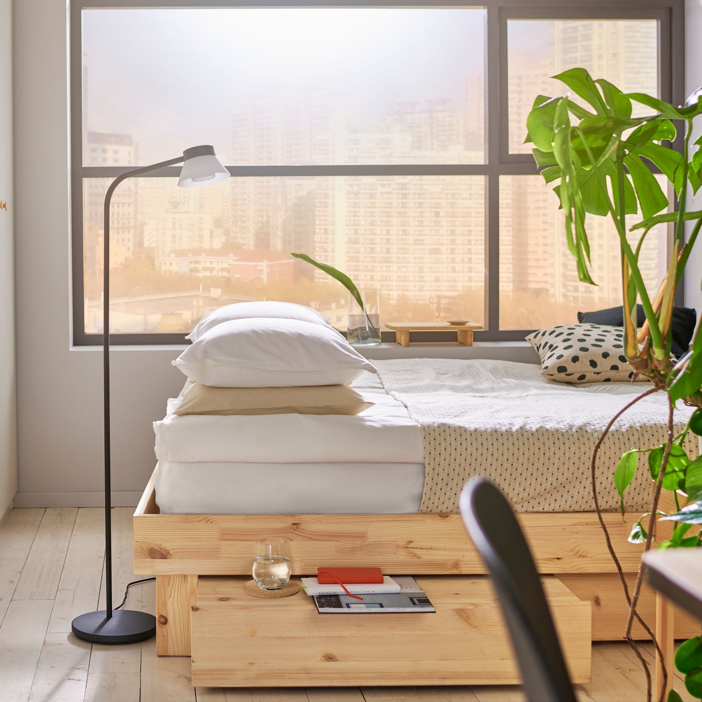 Bedroom with big window, GLAMBERGET bed in untreated wood with drawer underneath, beige bedding, white wardrobes to the left.