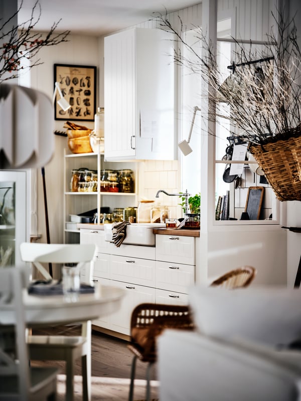 A bright country-style kitchen with white cabinets, a wooden counter top, an open shelf and decorative dried branches.