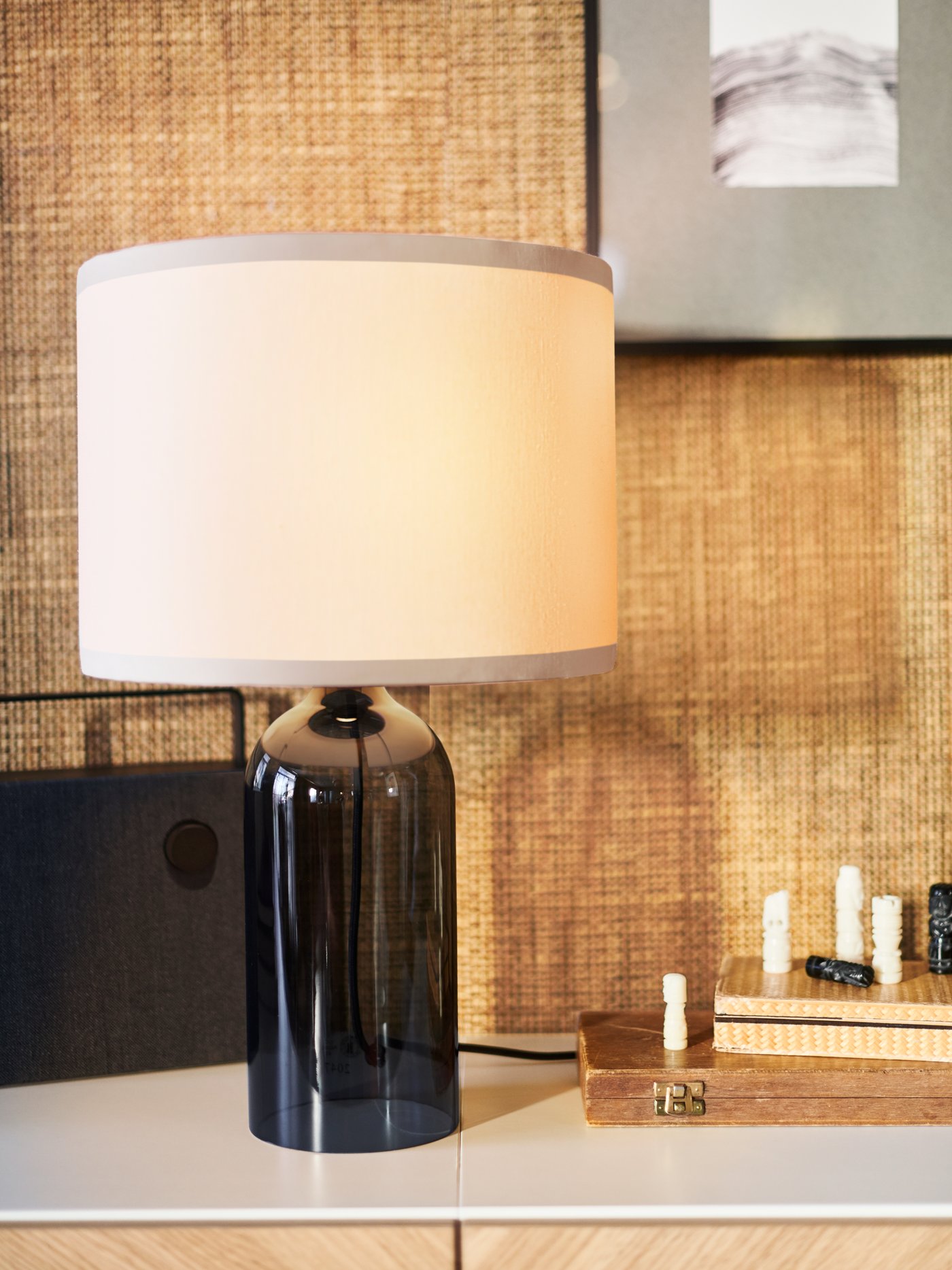 A TONVIS table lamp with a smoked glass base and white shade on a white surface beside a black ENEBY Bluetooth speaker.