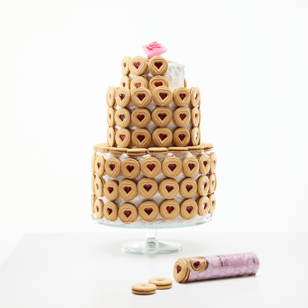 Gâteau recouvert de biscuits en forme de cœur avec garniture rouge, sur plateau en verre, avec biscuits à côté.