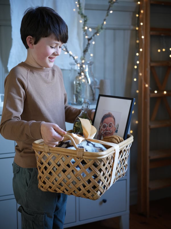 Een jong kind houdt een INSVEP mand met daarin allerlei cadeaus vast terwijl hij lacht naar de mand.