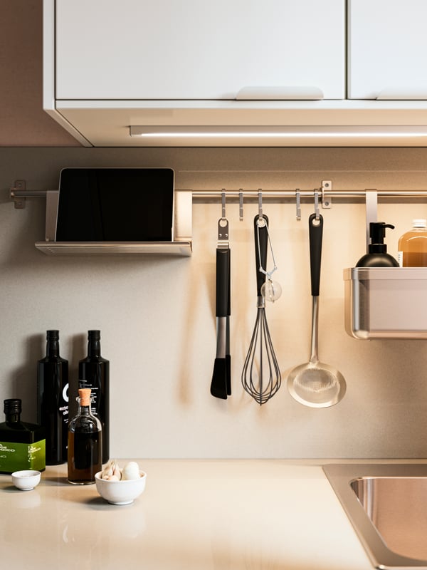 Una cocina con una barra KUNGSFORS debajo de un gabinete de cocina. En la barra cuelgan artículos de cocina como un cucharón, unas pinzas y un revolvedor.