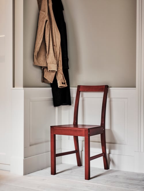 Hallway area featuring a red chair placed under two clothing items hanging from a beige wall. The chair is on a white floor.