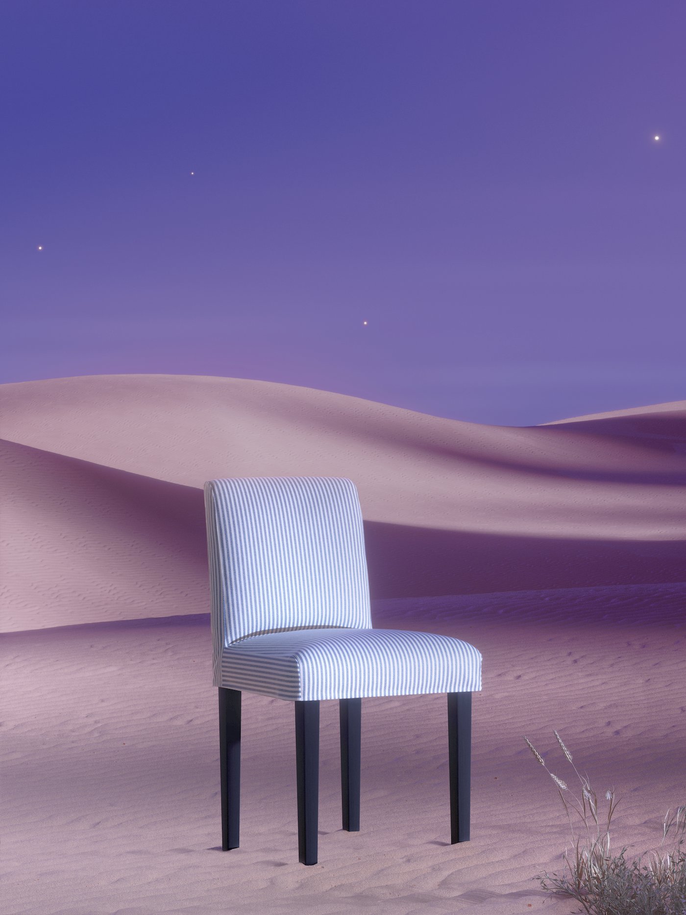 A white and blue-striped BERGMUND chair, with black legs, stands on sand in a violet-coloured desert landscape.