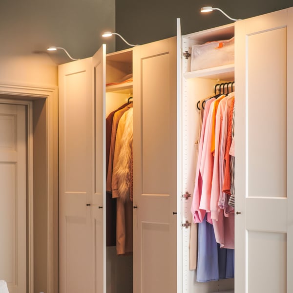 Two white PAX/GRIMO wardrobes with YTBERG cabinet lighting stand side by side against a wall near a door.