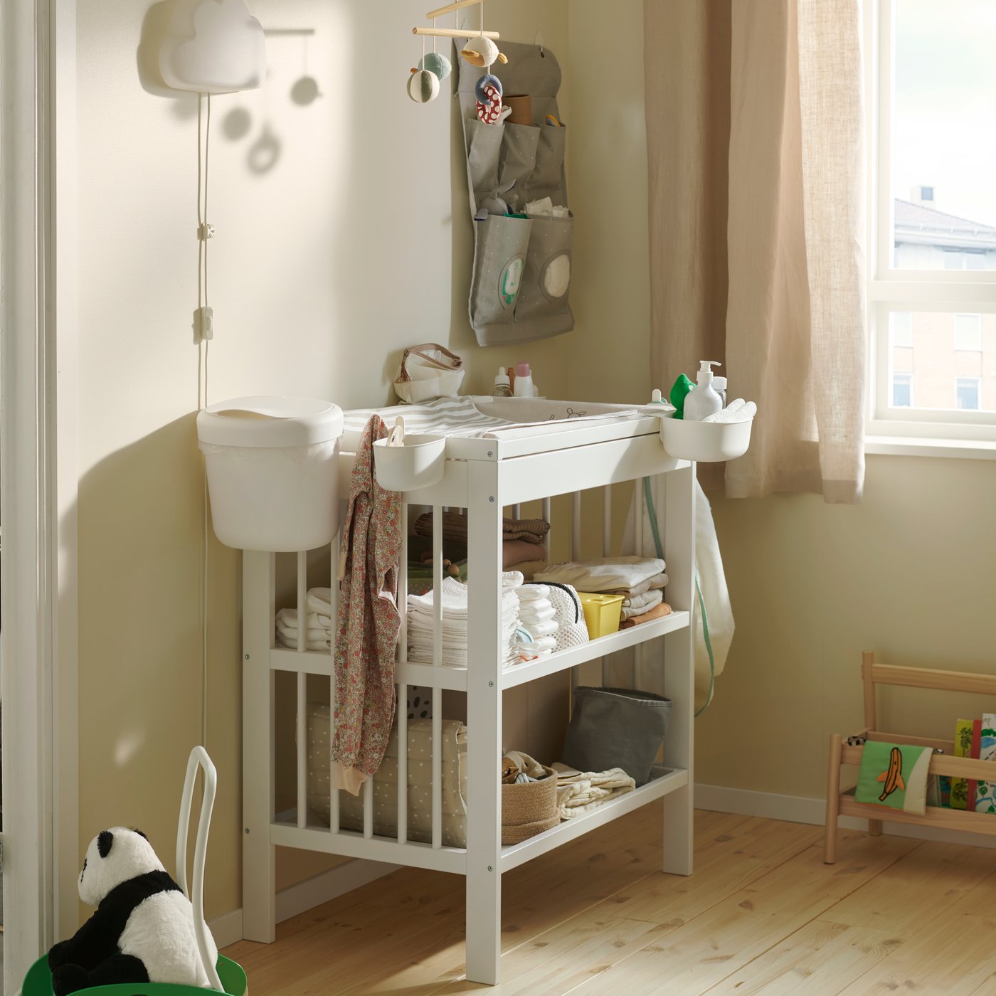 Ett barnrum med beige väggar och ett GULLIVER skötbord, vars hyllor är fyllda med blöjor och babyartiklar.
