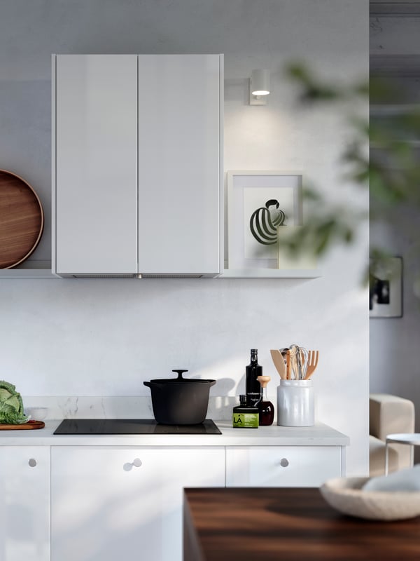 A SKÅDIS pegboard with notes and other things attached to it is placed on a kitchen wall with hooks with bags below it.