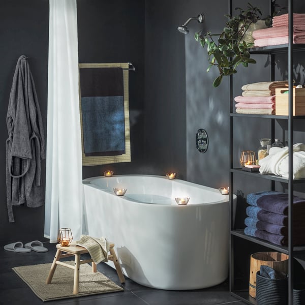 Bañera con velas encendidas y un banco con toallas para momento spa.