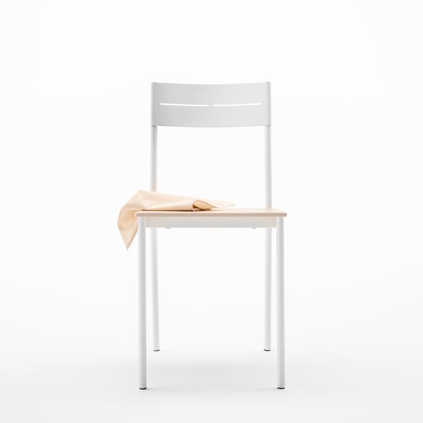A BUSLÄTT dining chair, with sleek white metal frame and seat in solid pine wood. On top of the seat, there’s a napkin.