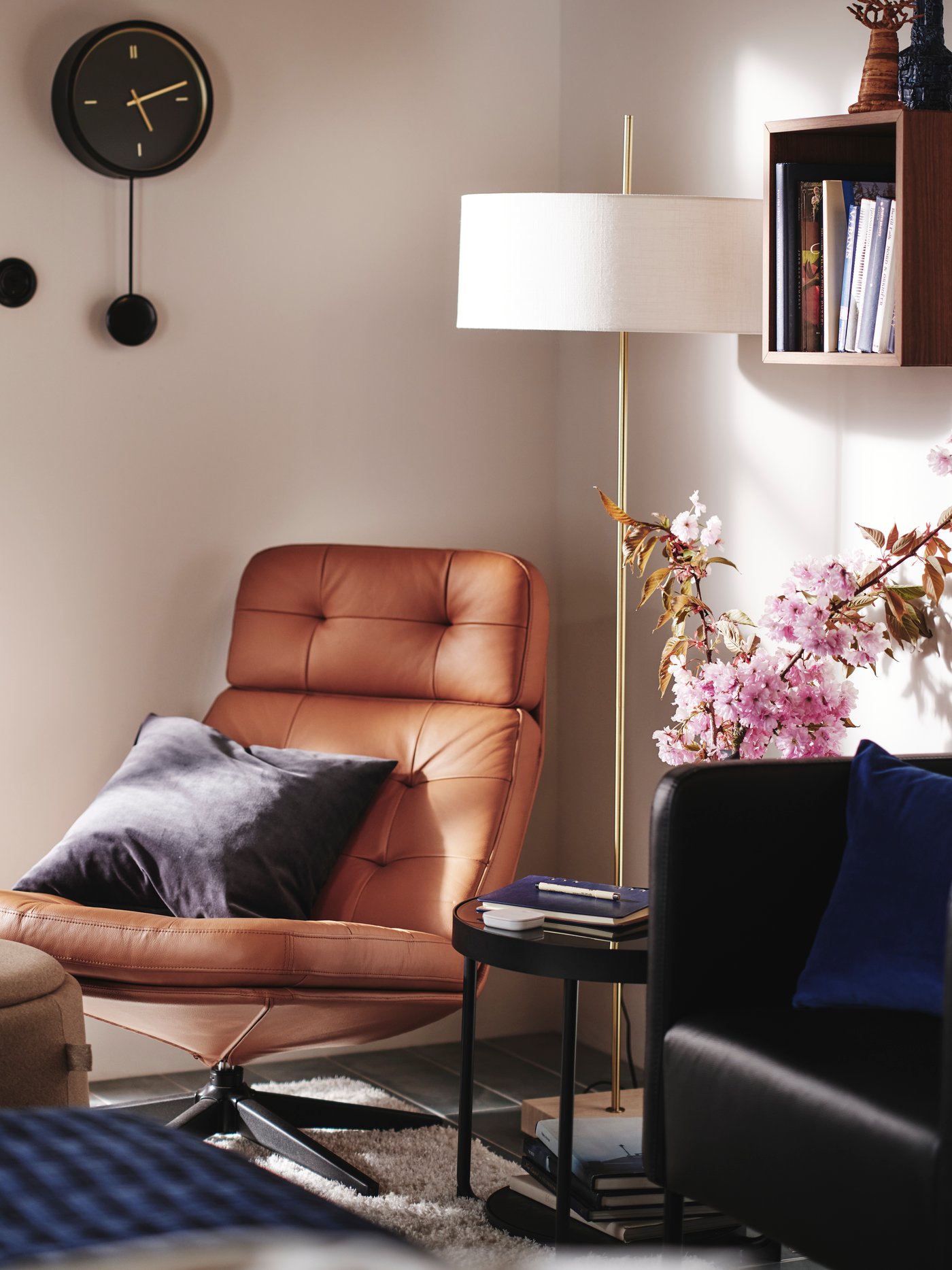 A corner of a bedroom with HAVBERG armchair in light brown, STOCKHOLM 2025 floor lamp and STURSK wall clock on the wall.