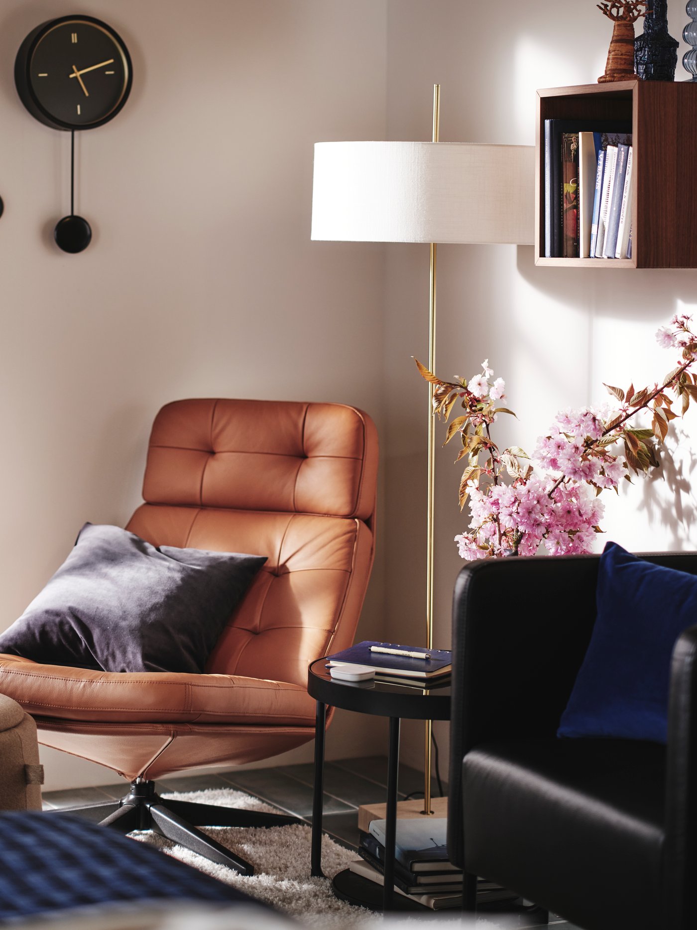 Ett hörn av ett sovrum med HAVBERG fåtölj i ljusbrunt, STOCKHOLM 2025 golvlampa och STURSK väggklocka på väggen.