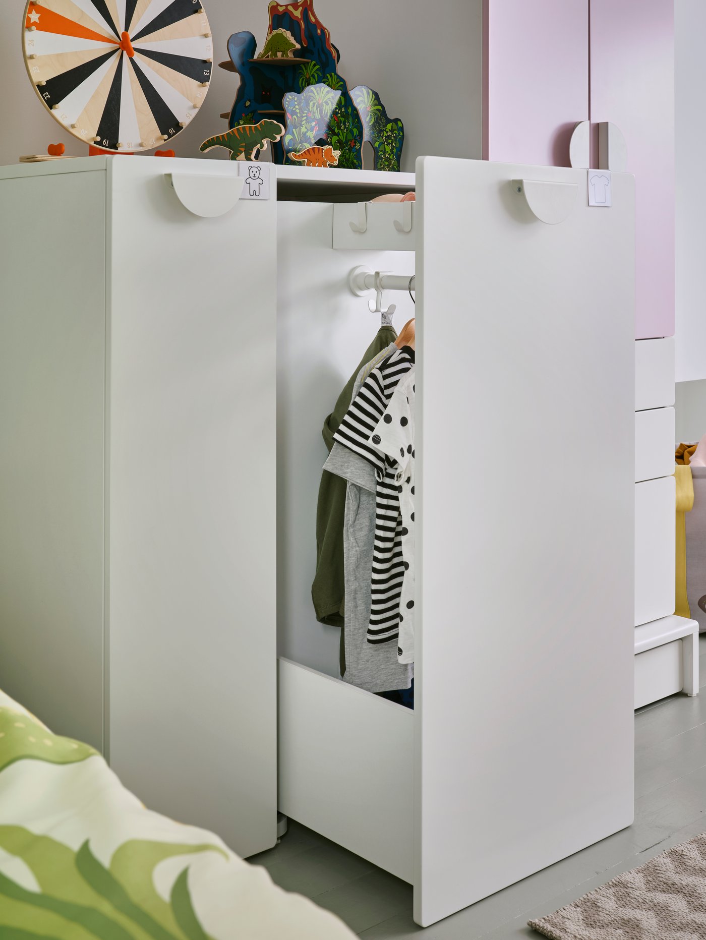 A SMÅSTAD wardrobe with a pull-out unit stands open. Hooks and a clothes rail with clothes on hangers are inside.