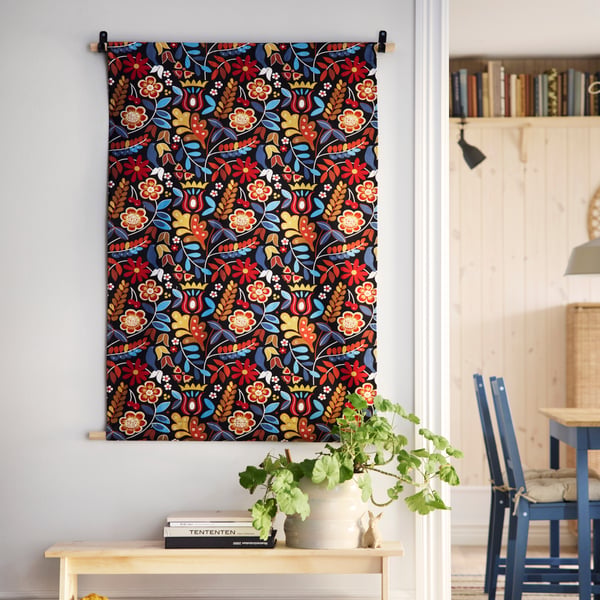 A wall decoration made from BLÅRAPUNKEL pre-cut fabric hangs on a wall above a plant in a beige HASSELBUKETT plant pot.