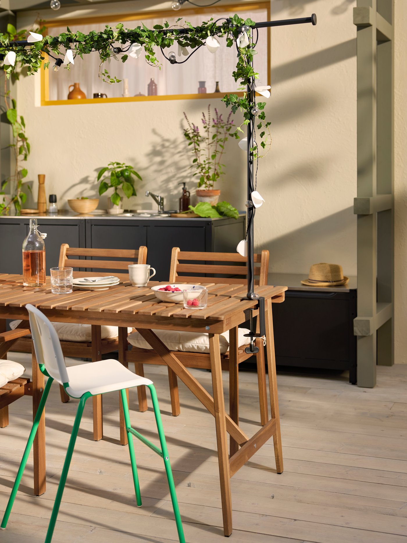A patio with a dark brown ASKHOLMEN outdoor table, outdoor chairs with armrests, and a highchair surrounded by plants.
