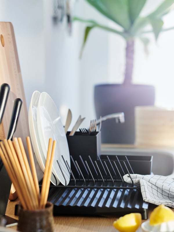 A black dish drainer with a kitchen utensil rack and a plate holder, two white plates, wooden chopsticks and a tea towel.
