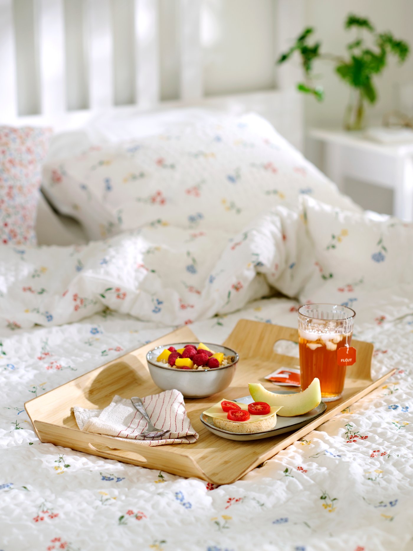 Close-up of a breakfast in bed with fruit, tea and a sandwich served on SILVERHAJMAL tray on top of PILDVÄRGMAL duvet cover.