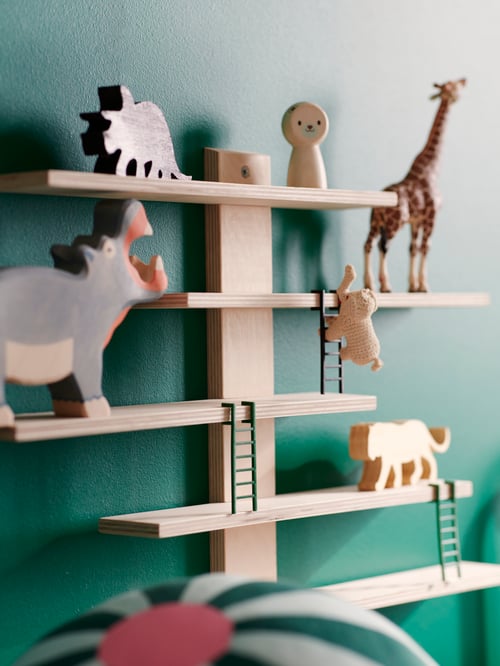 Children's room with green wall, wooden wall shelf, placed on the wall and wooden toys shaped as animals, displayed on shelf.