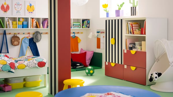 Una combinación de almacenaje SMÅSTAD/PLATSA roja/de rayas con tres cajones enfrente de un pilar en una habitación infantil.