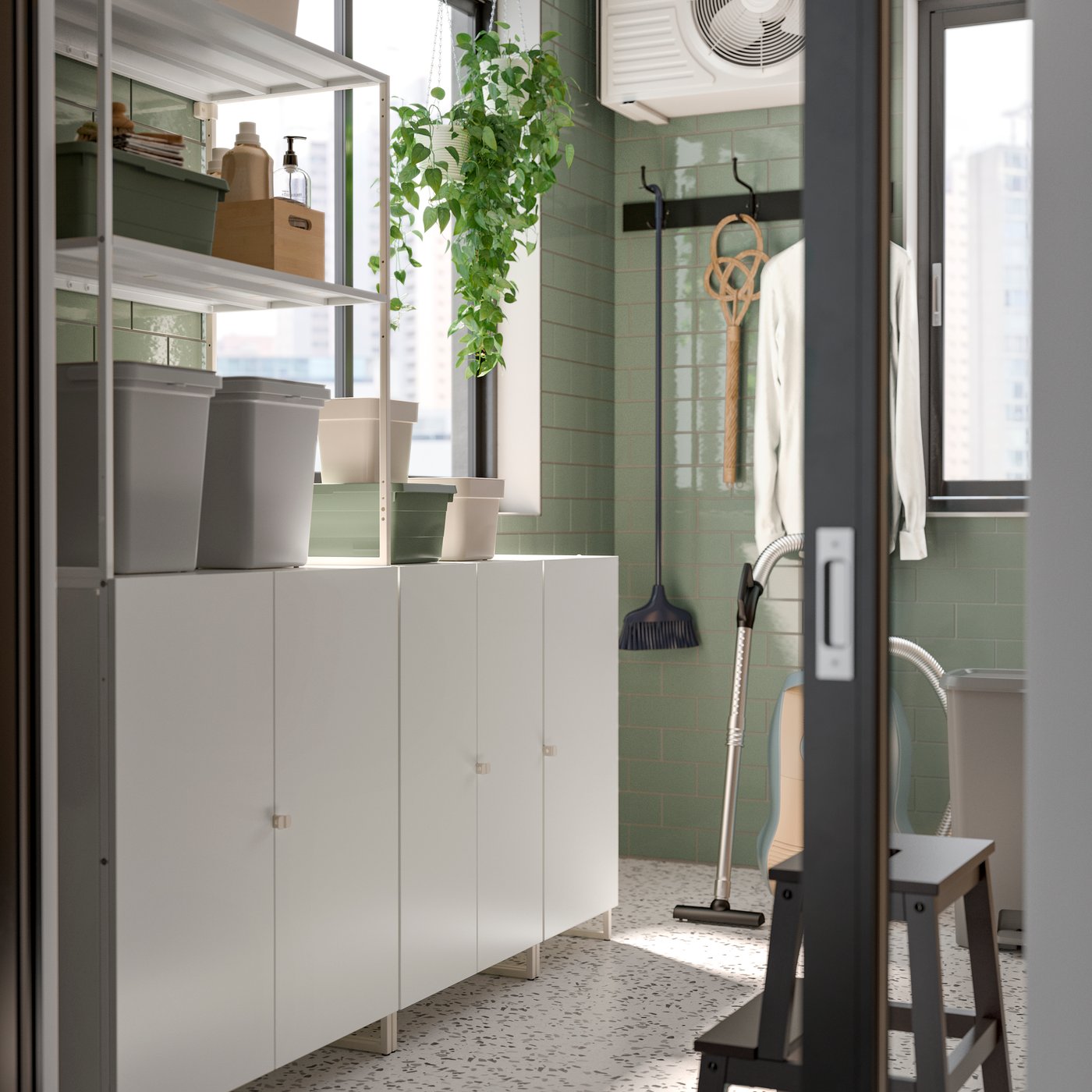 A bright, modern storage area features open shelves JOSTEIN with boxes, a hanging plant, and cleaning items near a window.
