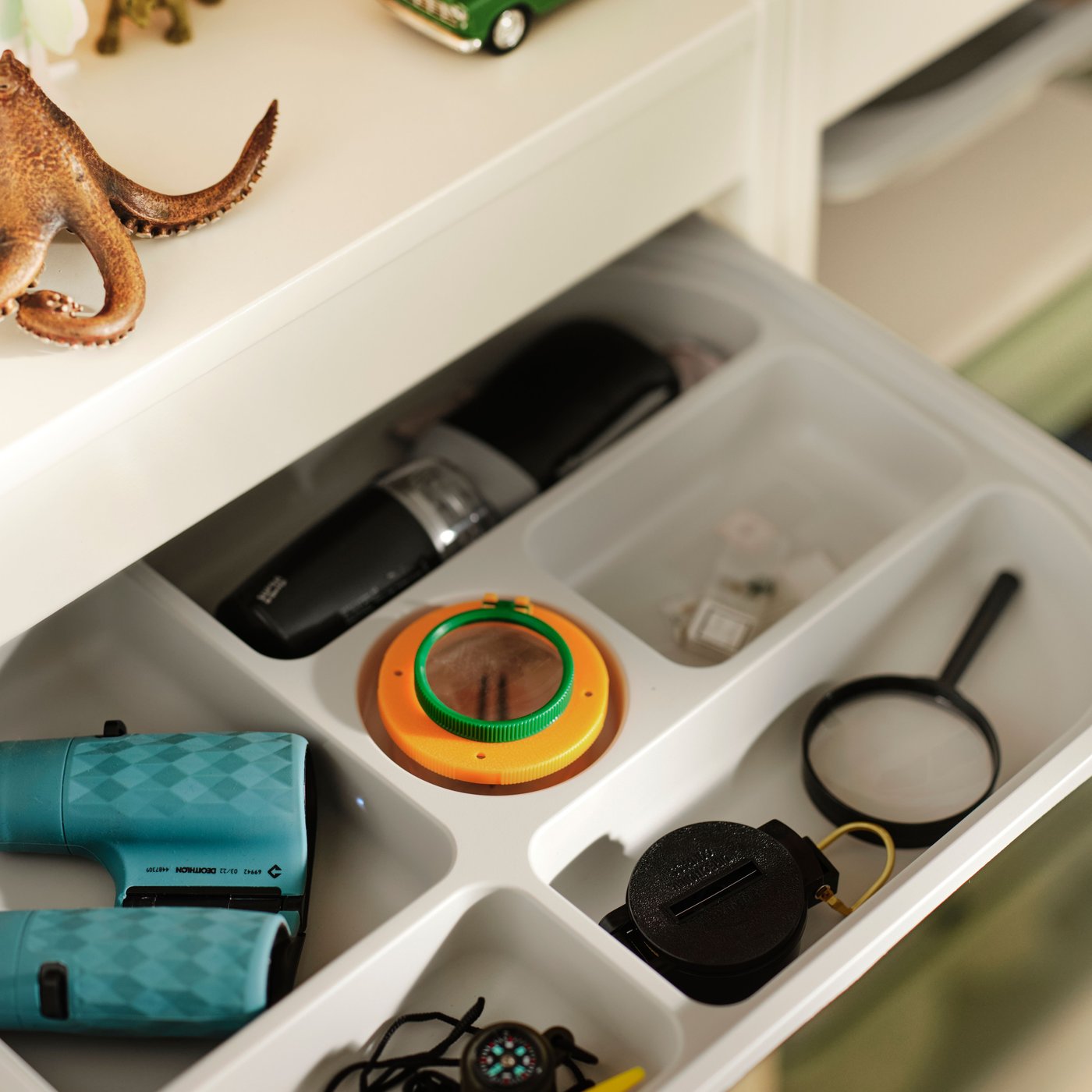 درج أبيض صغير مسحوب مليء به أغراض أطفال متنوعة مرتبة في أقسام. دمى حيوانات في الأعلى