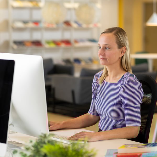 デスクに座ったイケアのコワーカーが、パソコン画面を見ながら書類と観葉植物のあるワークスペースで作業している
