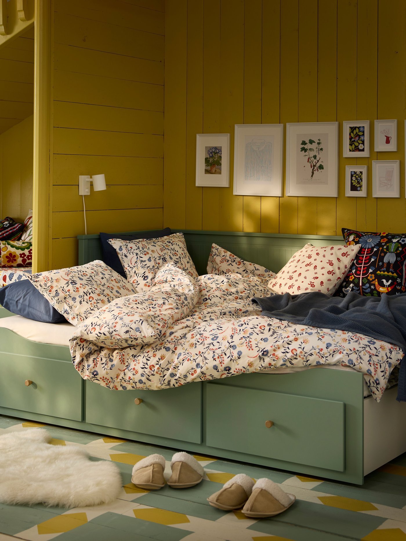 En grågrøn HEMNES sovesofa med tre skuffer og blomstret sengetøj og puder ser hyggelig og indbydende ud.