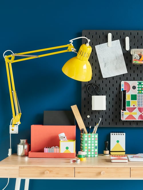 A bamboo LILLÅSEN desk with steel legs in a dark blue room and near a yellow adjustable-arm task-lighting lamp.