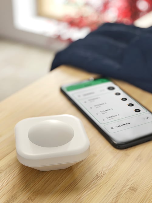 RÅGRUND ローグルンドベンチの上に置いたホワイトのVALLHORN ヴァルホルン ワイヤレスモーションセンサーとスマートフォンのクローズアップ。