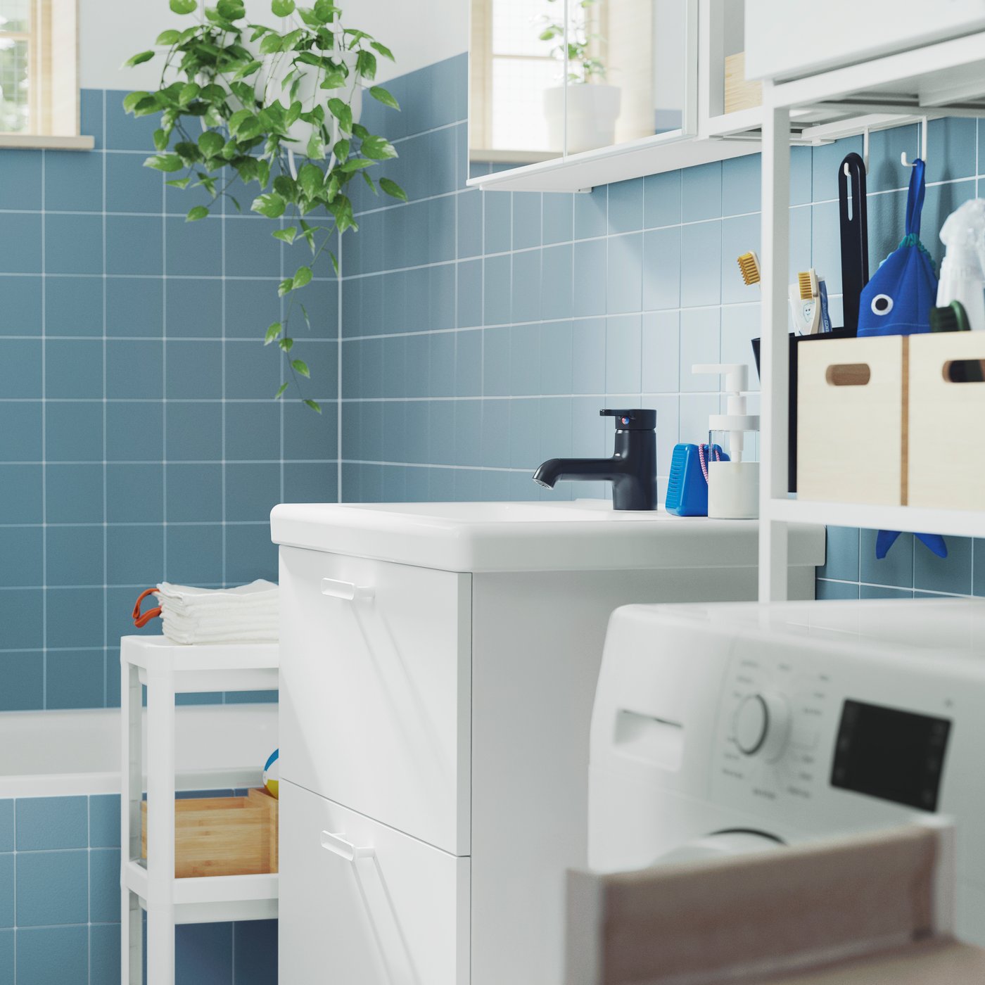 In un bagno con piastrelle blu e vasca, un mobile base ENHET bianco, un mobile a specchio con due ante e un carrello VESKEN.