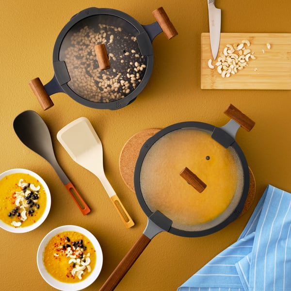 KLIPPFISK sauté pan with lid and a KLIPPFISK pan with lid and an APTITLIG chopping board in bamboo, white bowls of food.