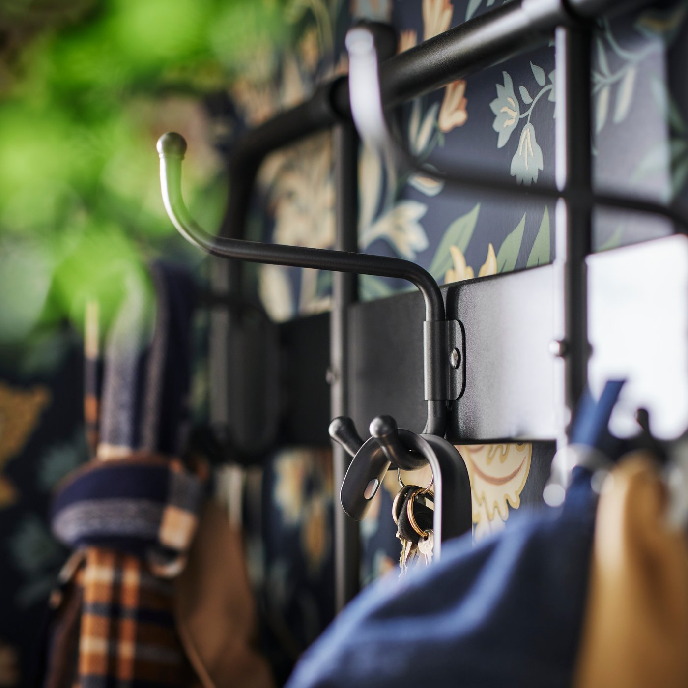 Es ist eine Nahaufnahme eines Hakens an einem schwarzen NIPÅSEN Garderobenständer mit Bank/Schuhaufbewahrung zu sehen. Daran hängen ein paar Schlüssel und ein Schuhlöffel.