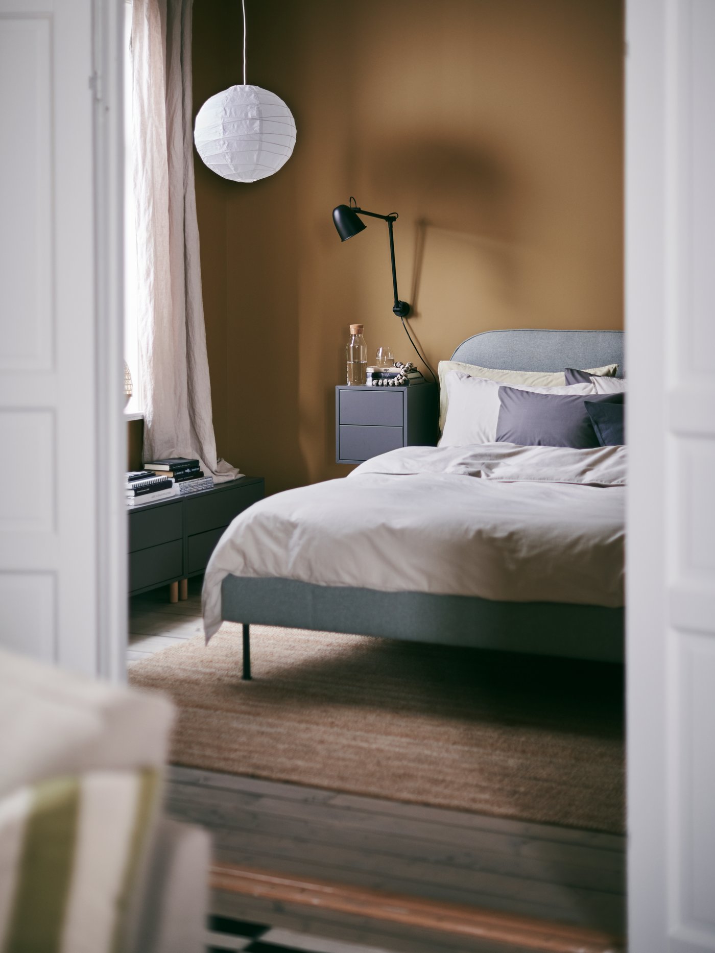 A glimpse into a warm and inviting bedroom with a VADHEIM bed and REGOLIT pendant lamp shade made from paper.