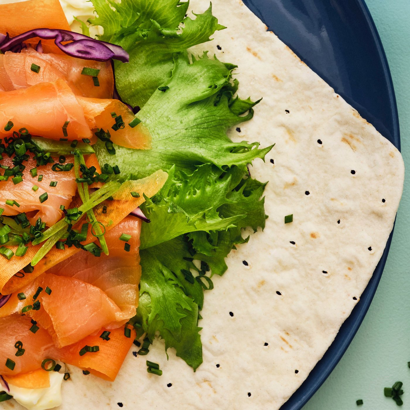 GRÄDDAT soft thin flatbread topped with SJÖRAPPORT cold-smoked salmon, lettuce, and purple cabbage, served on a blue plate.
