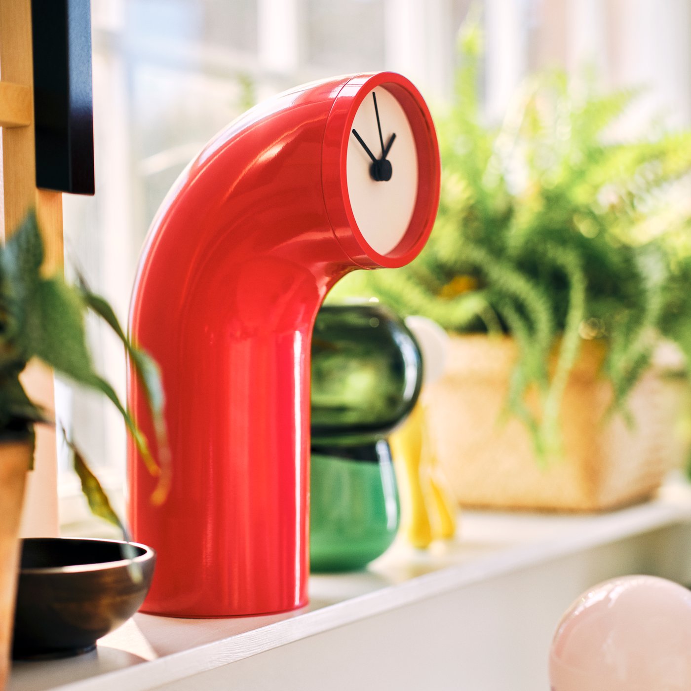 A red IKEA PS 2026 table clock sitting on a windowsill in a living room.