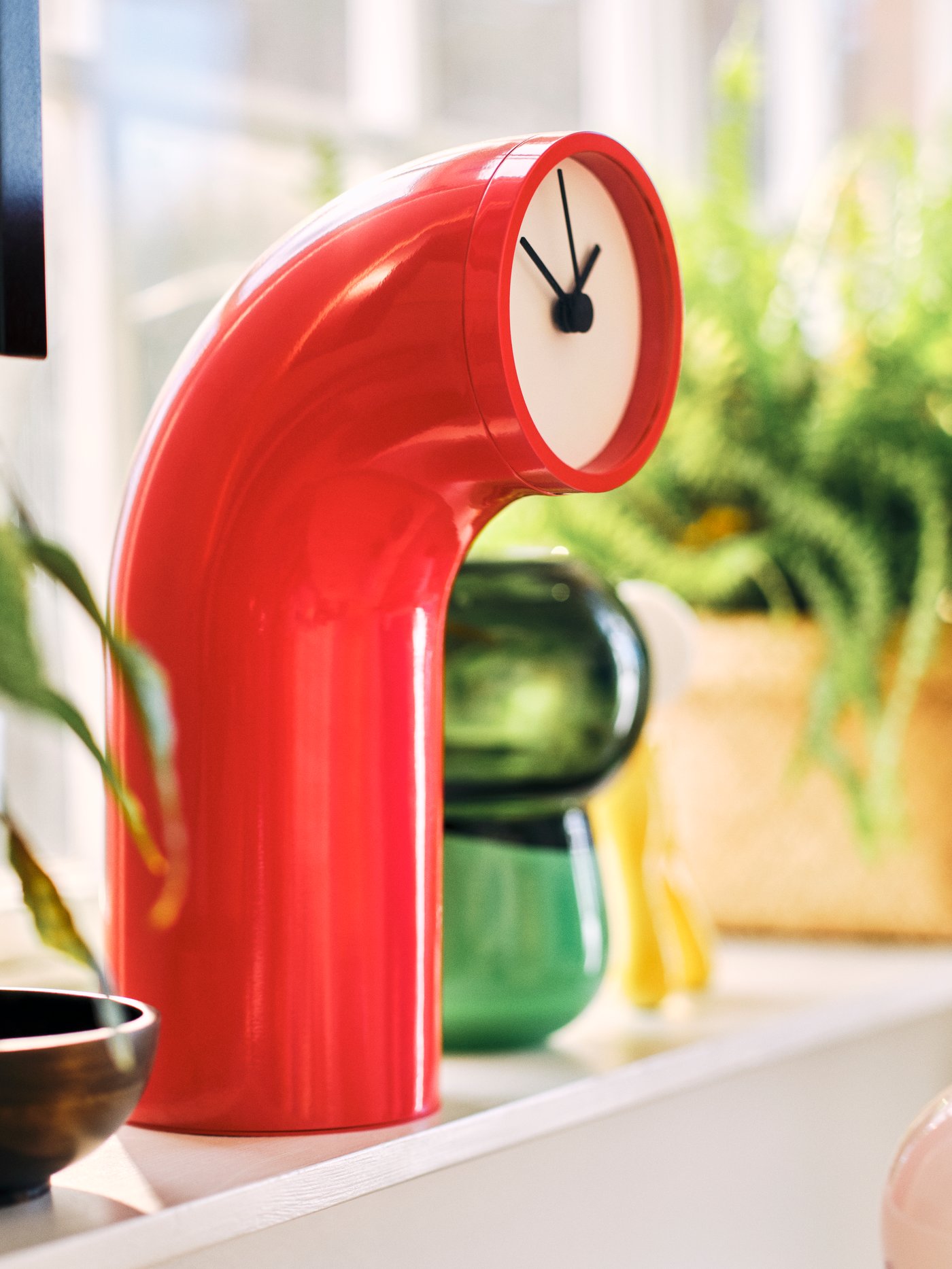 A red IKEA PS 2026 table clock sitting on a windowsill in a living room.
