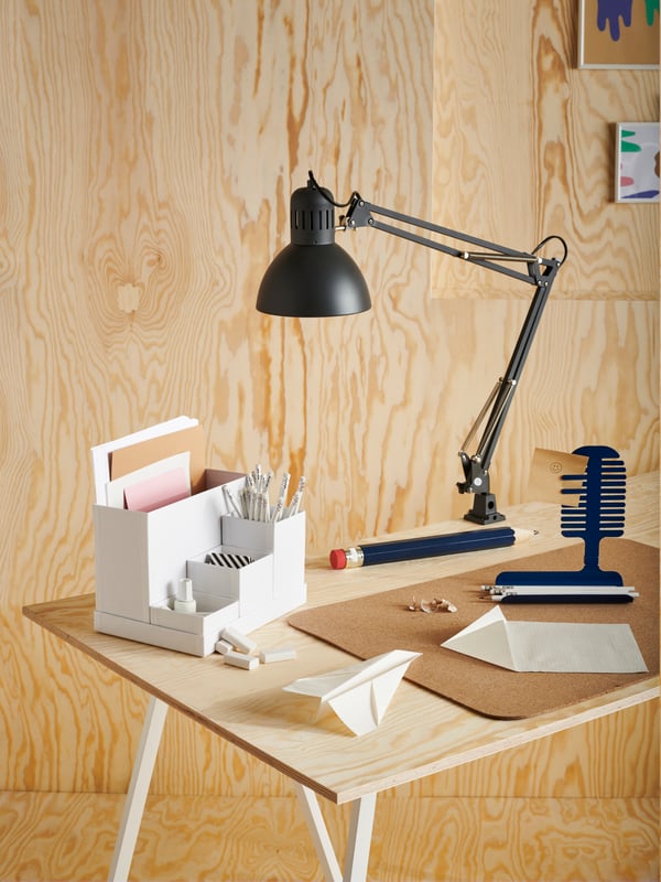 A white work lamp with wireless charging, a black phone, white pegboards, a pair of headphones, a grey-turquoise desk.
